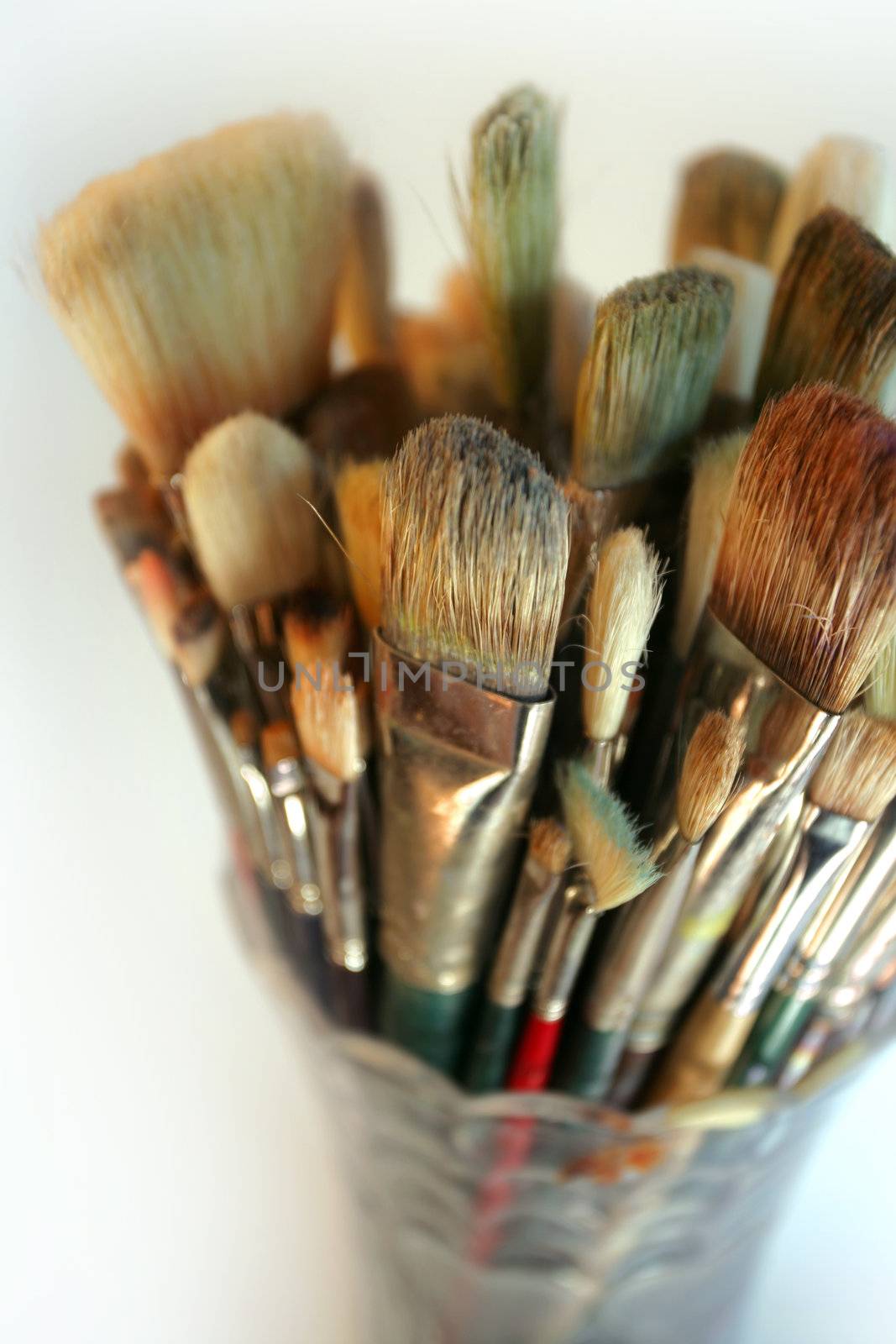 A very shallow depth-of-field image of used paintbrushes stacked in a glass vase. Focus is on the front brushes.
