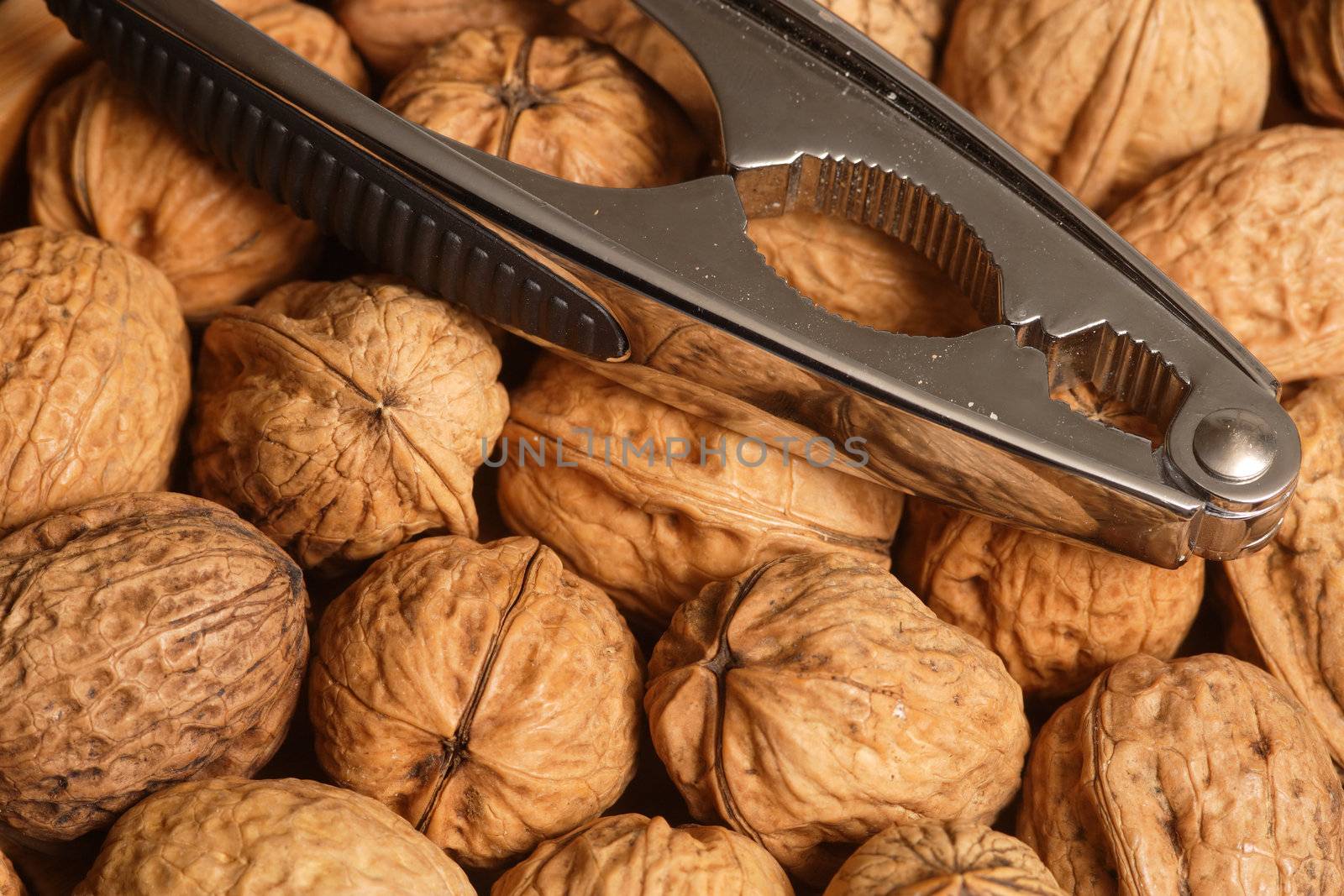 Group of walnuts with nutcracker resting on top.
