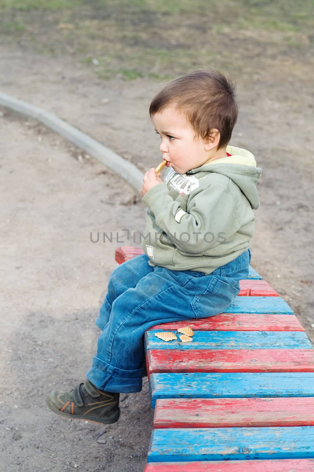 Boy eating cookie and relaxing (sitting on bench in park)