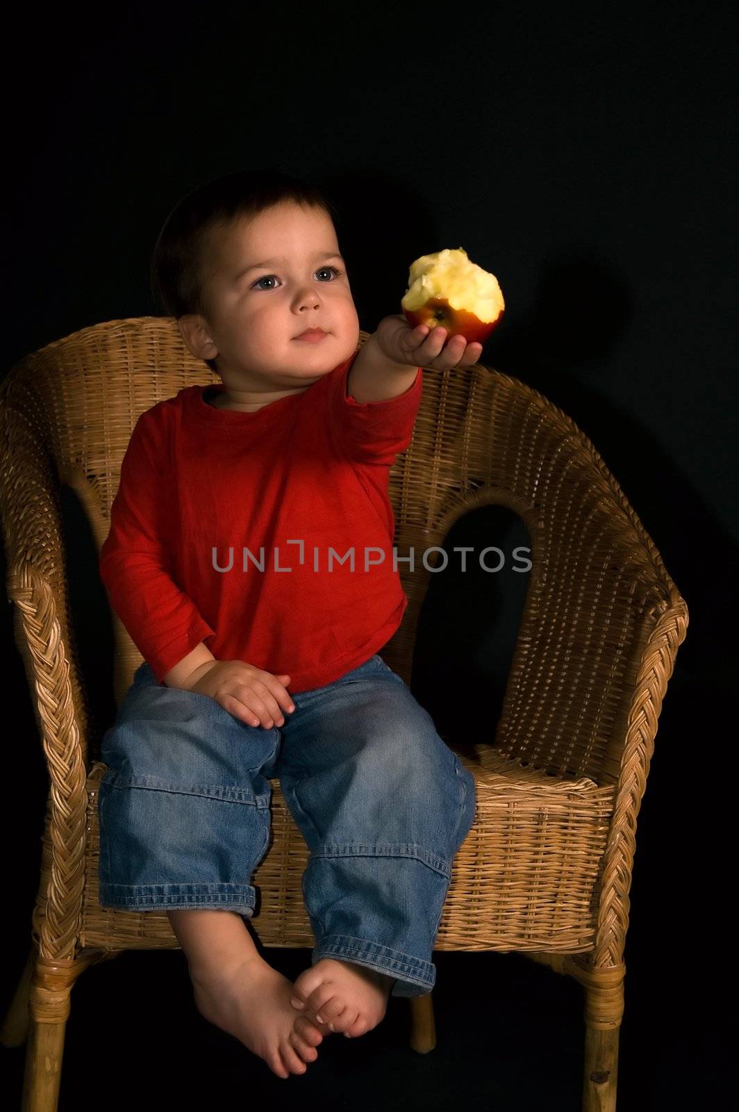 Child sitting in tha armchair and giving apple (isolated on black)