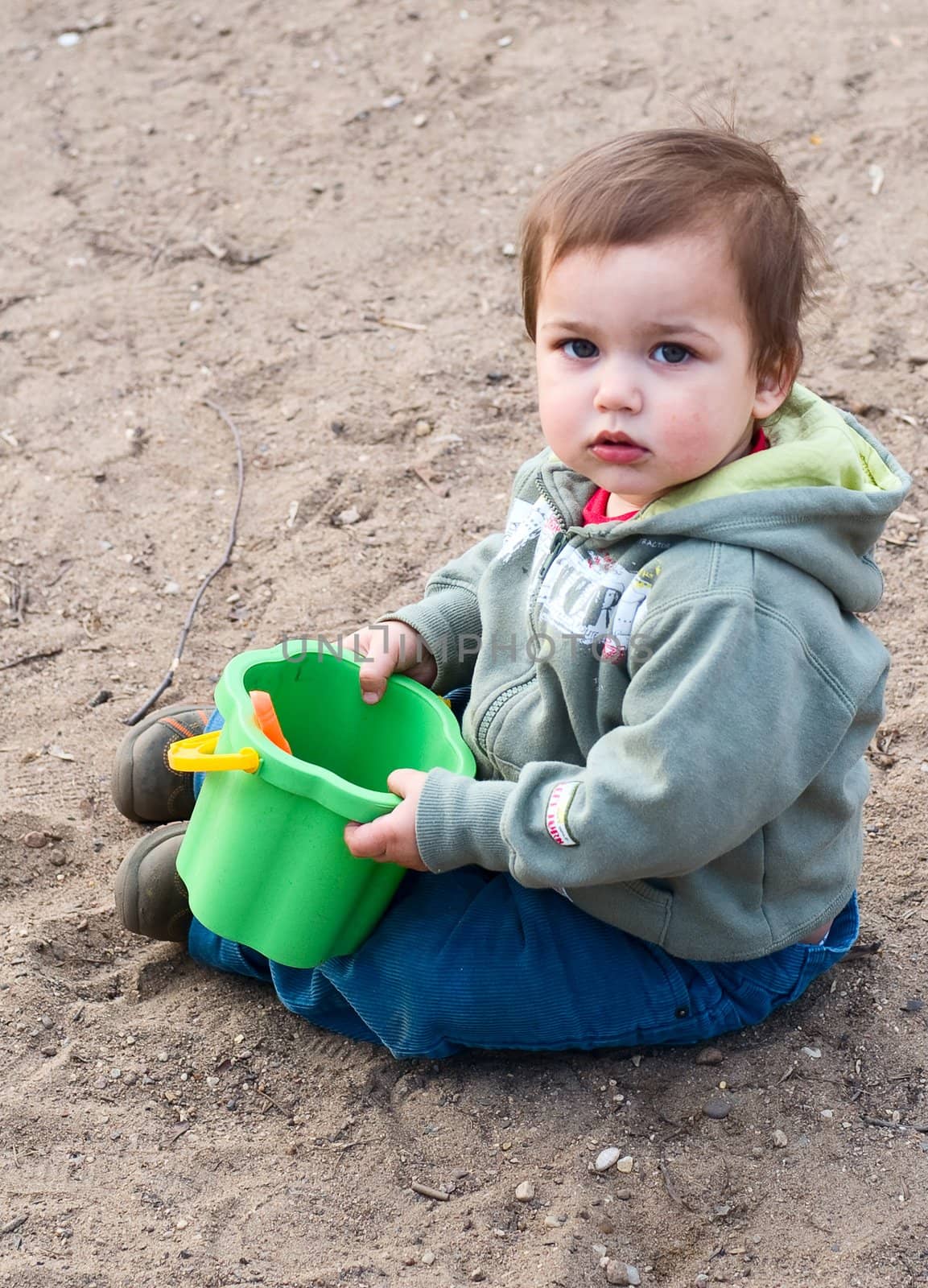 thoughtful boy in green dress with bucket sitting on sand