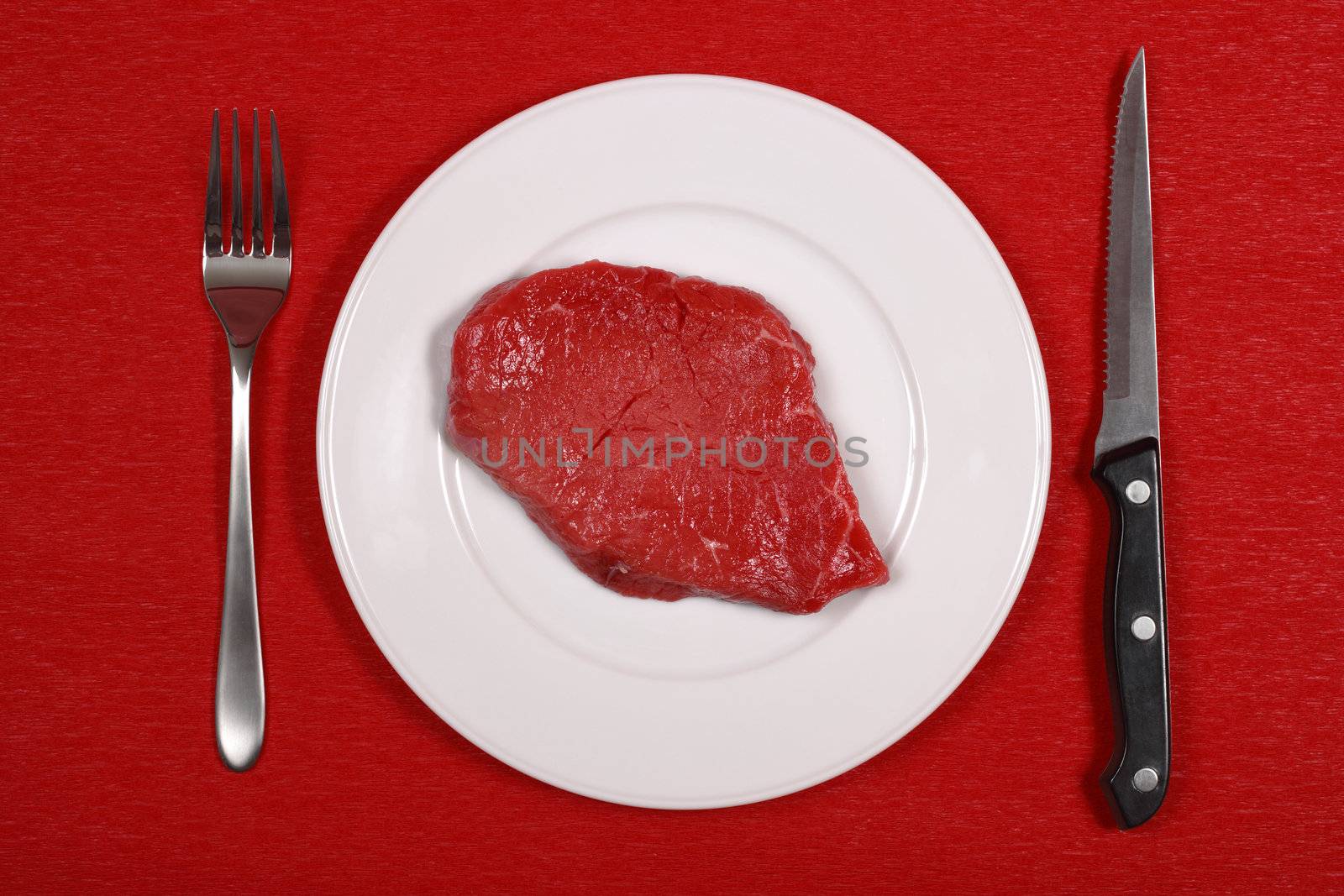 Raw meat on a dinner plate with knife and fork.
