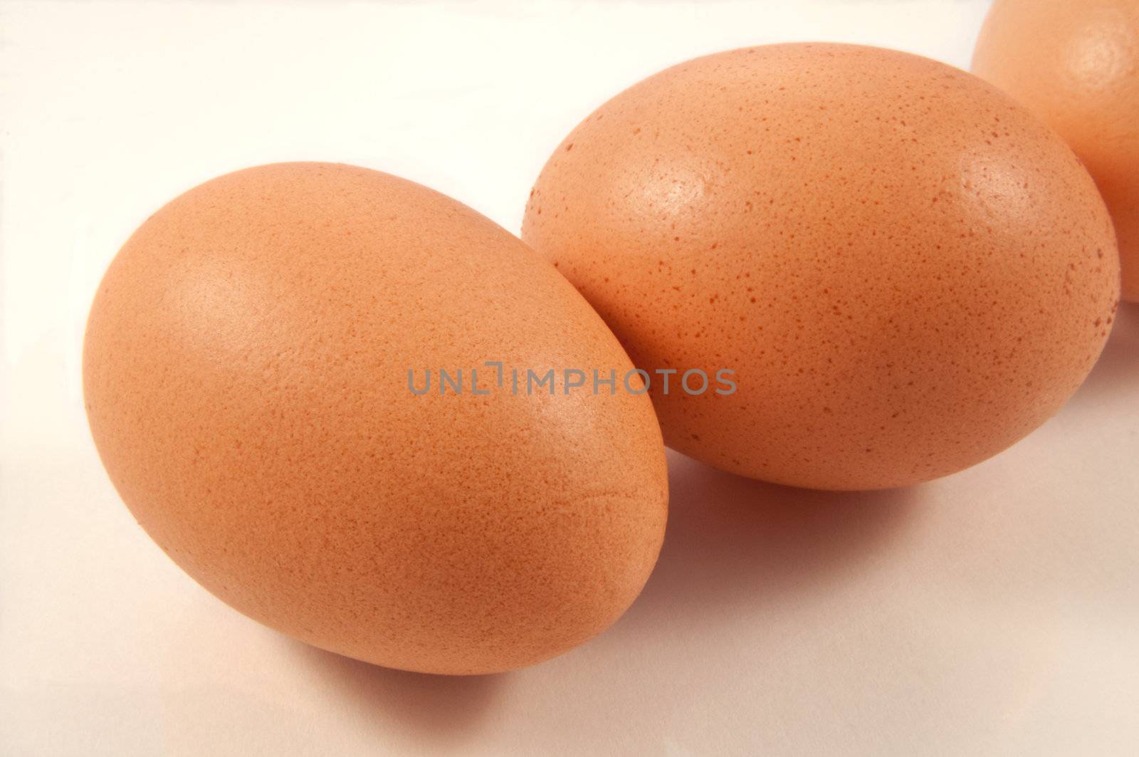 Close up and low level angle of several fresh brown eggs arranged over white.