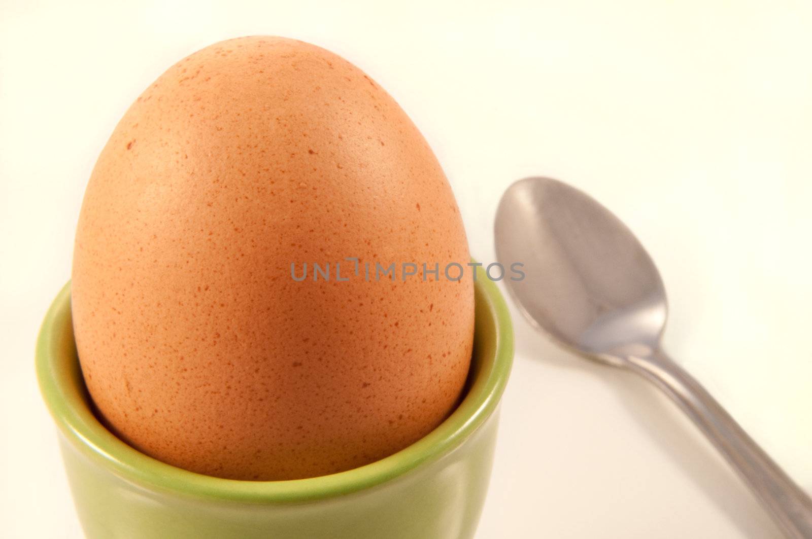 Close up of a boiled egg arranged in a lime green ceramic eggcup with white background and silver spoon.