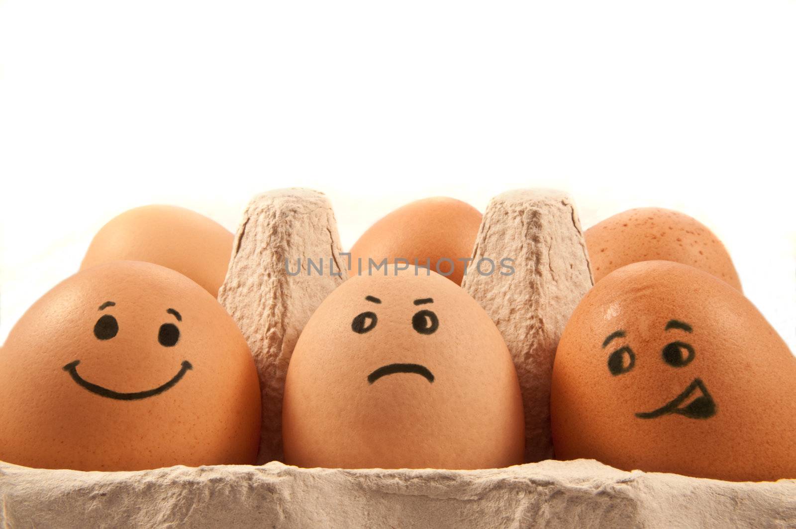 Close and low level capturing a group of brown eggs with painted human faces arranged in a cardboard carton with white background.