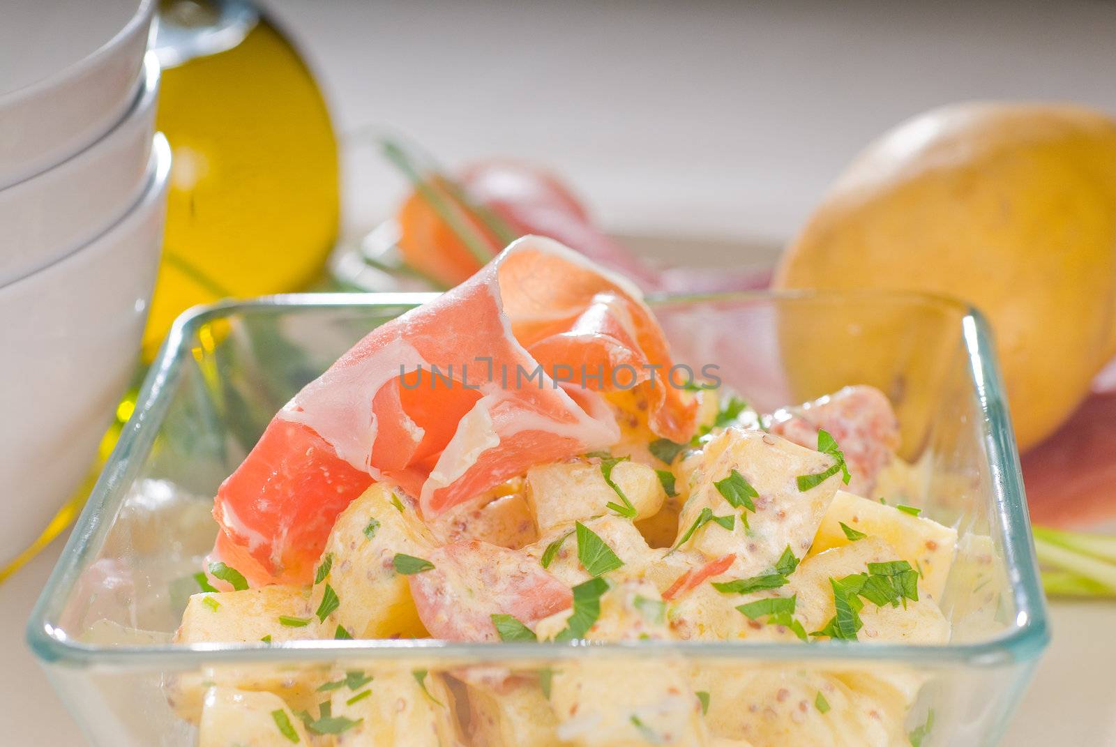 fresh home made parma ham and potato salad,with raw ingredients around with bowls and dishware on a table