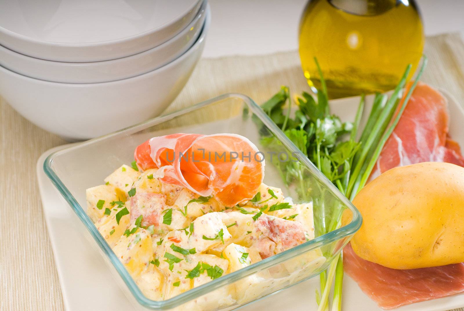 fresh home made parma ham and potato salad,with raw ingredients around with bowls and dishware on a table