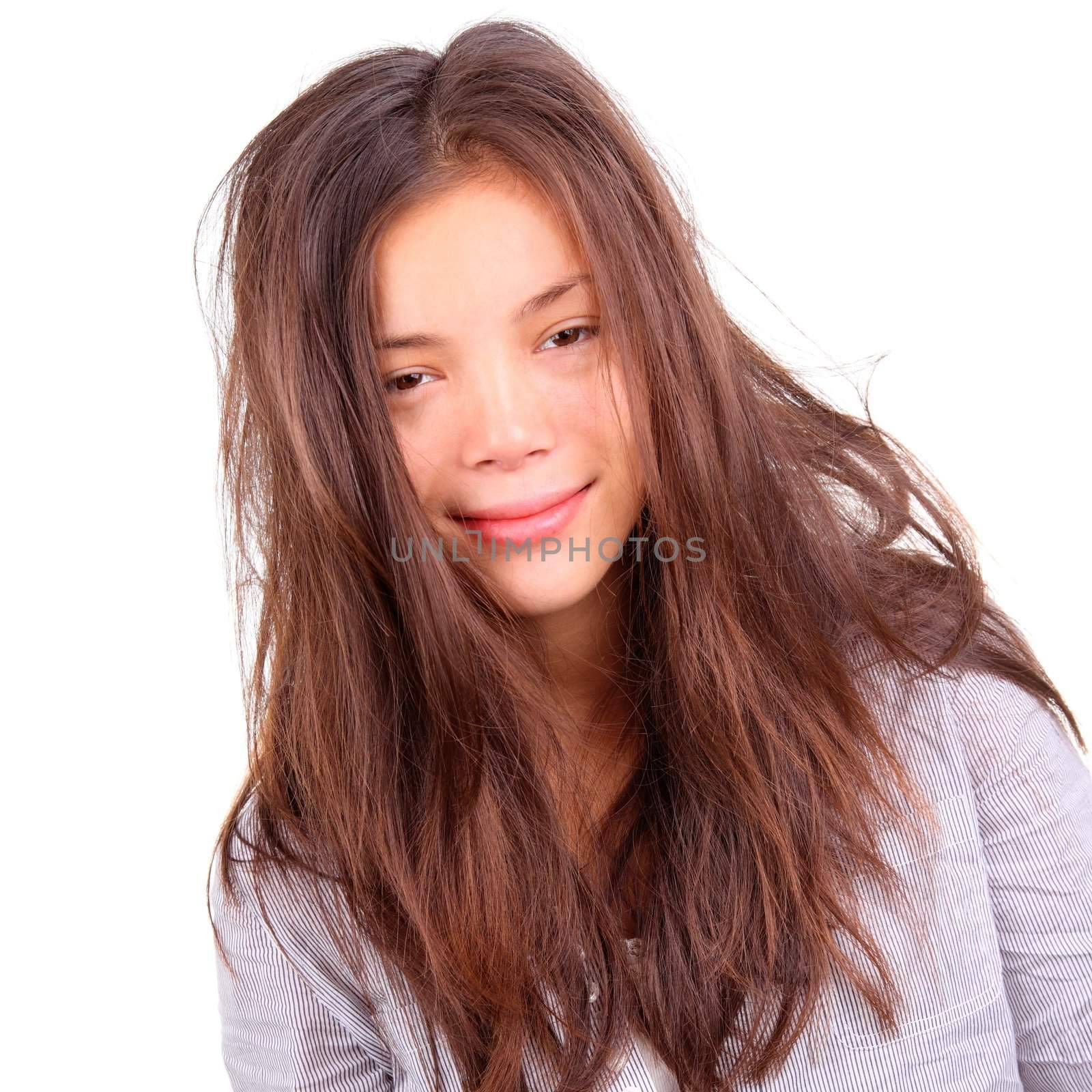 Tired woman portrait. Tired woman with very messy long morning hair and a silly smile - just out of bed. Beautiful mixed chinese / caucasian model isolated on white background.