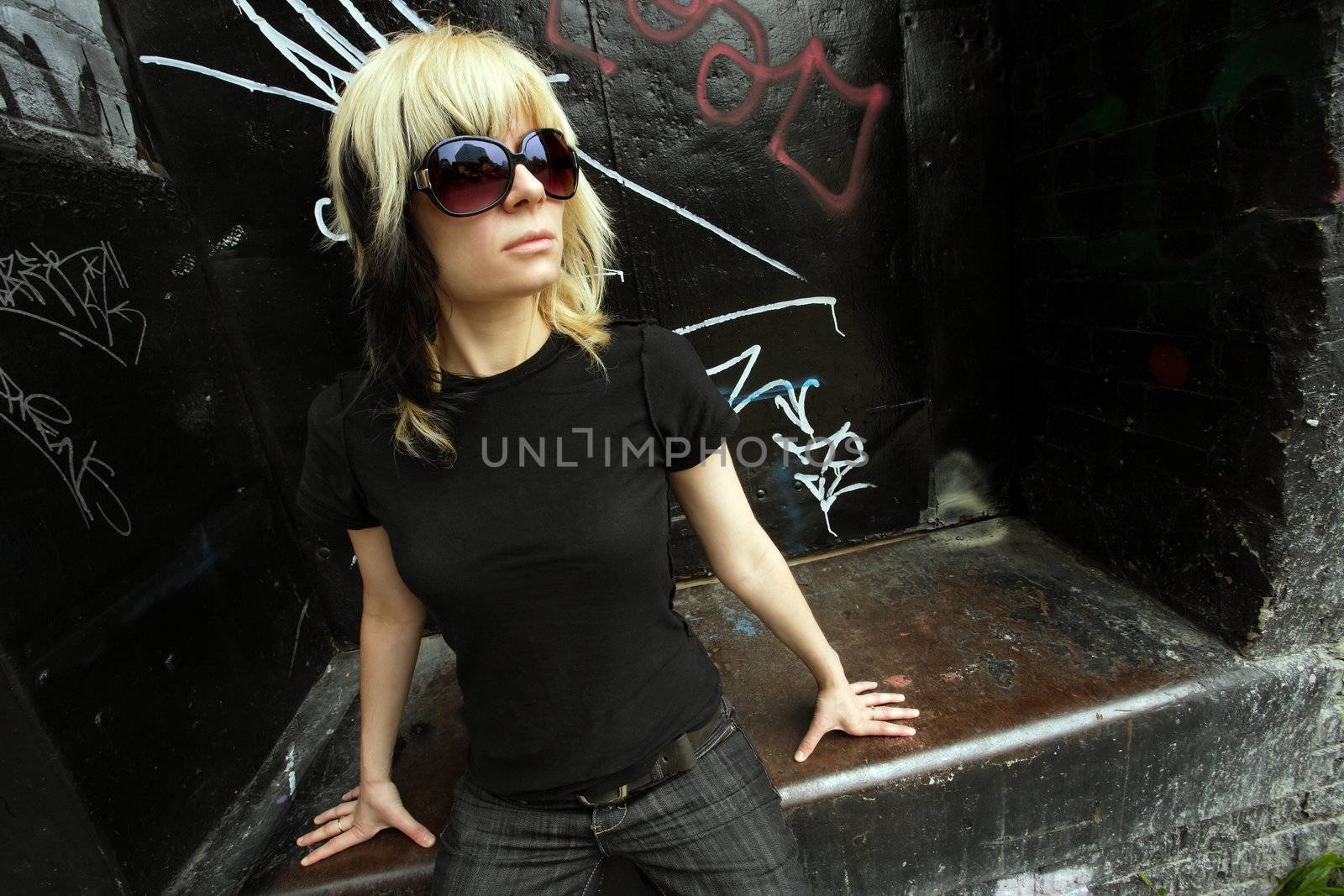 Beautiful young woman posing in the city wearing large sunglasses.
