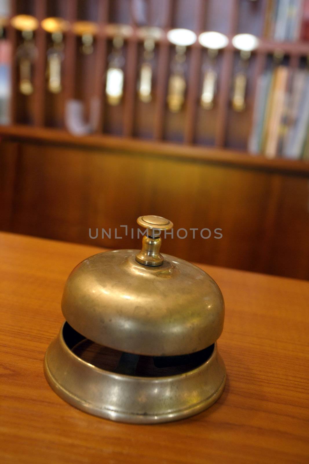 Vintage brass bell on hotel front desk with blurred key rack in the background. Very shallow depth of field with focus on the button.
