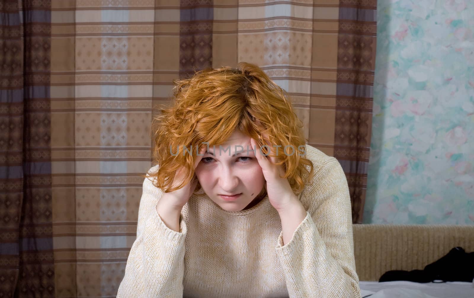 Young stressed woman sitting on the bed and hold her hand on own head