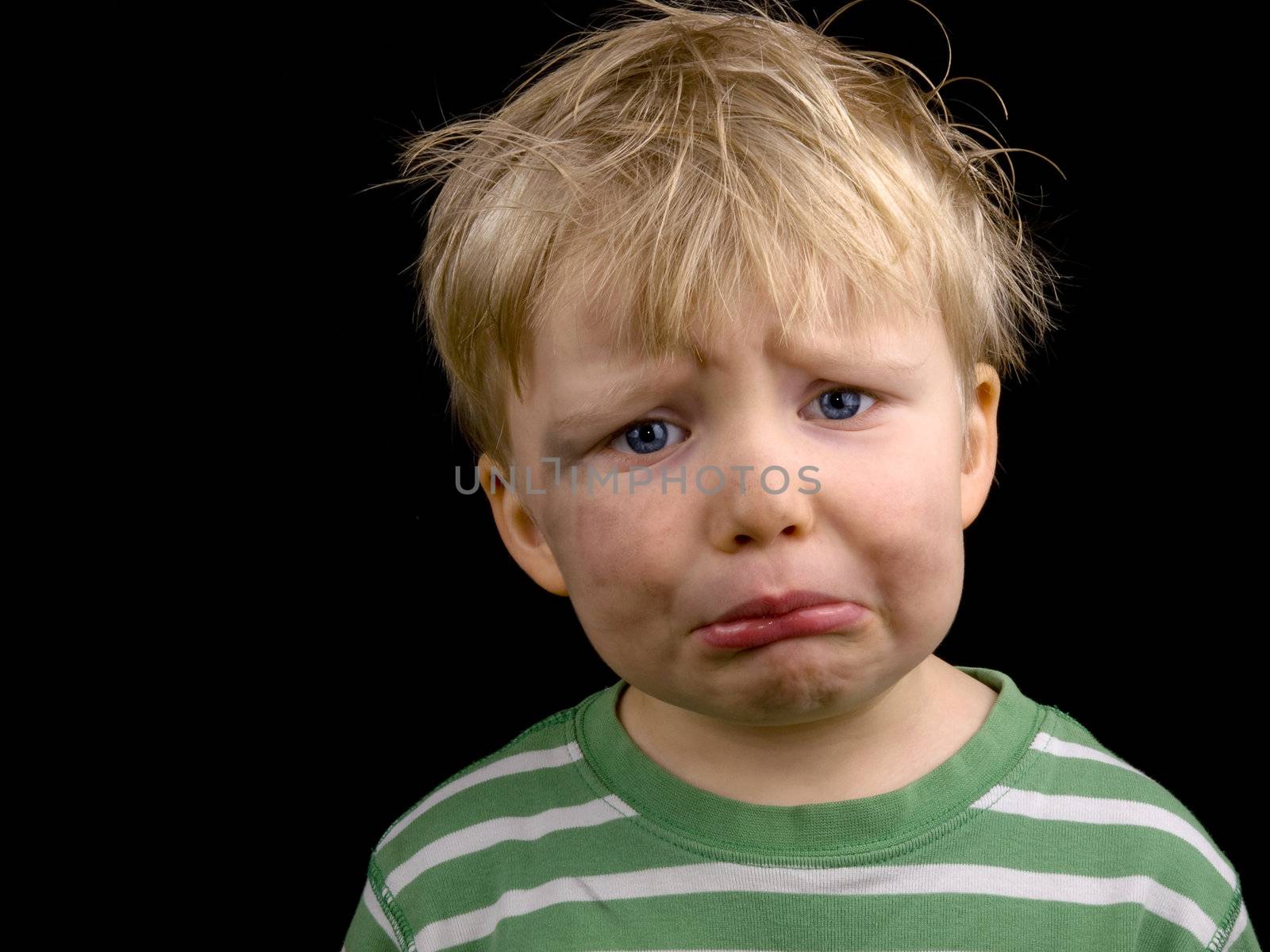 Sad little boy on black background. Boy have blond hair, blue eyes and a bit of dirt on face