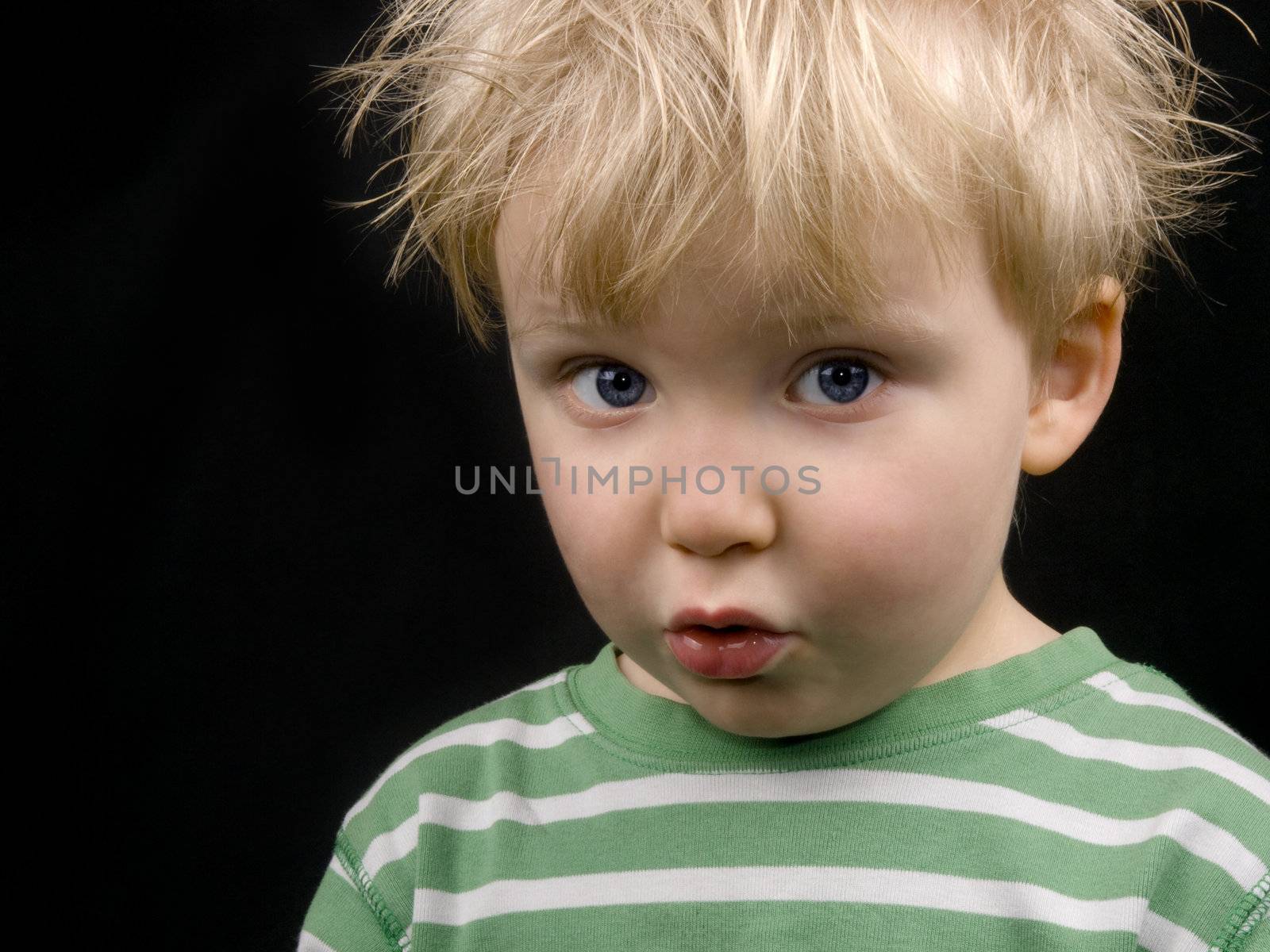 Little boy making funny face, on black background. Boy have blue eyes and blond hair and have a bit of dirt on his face