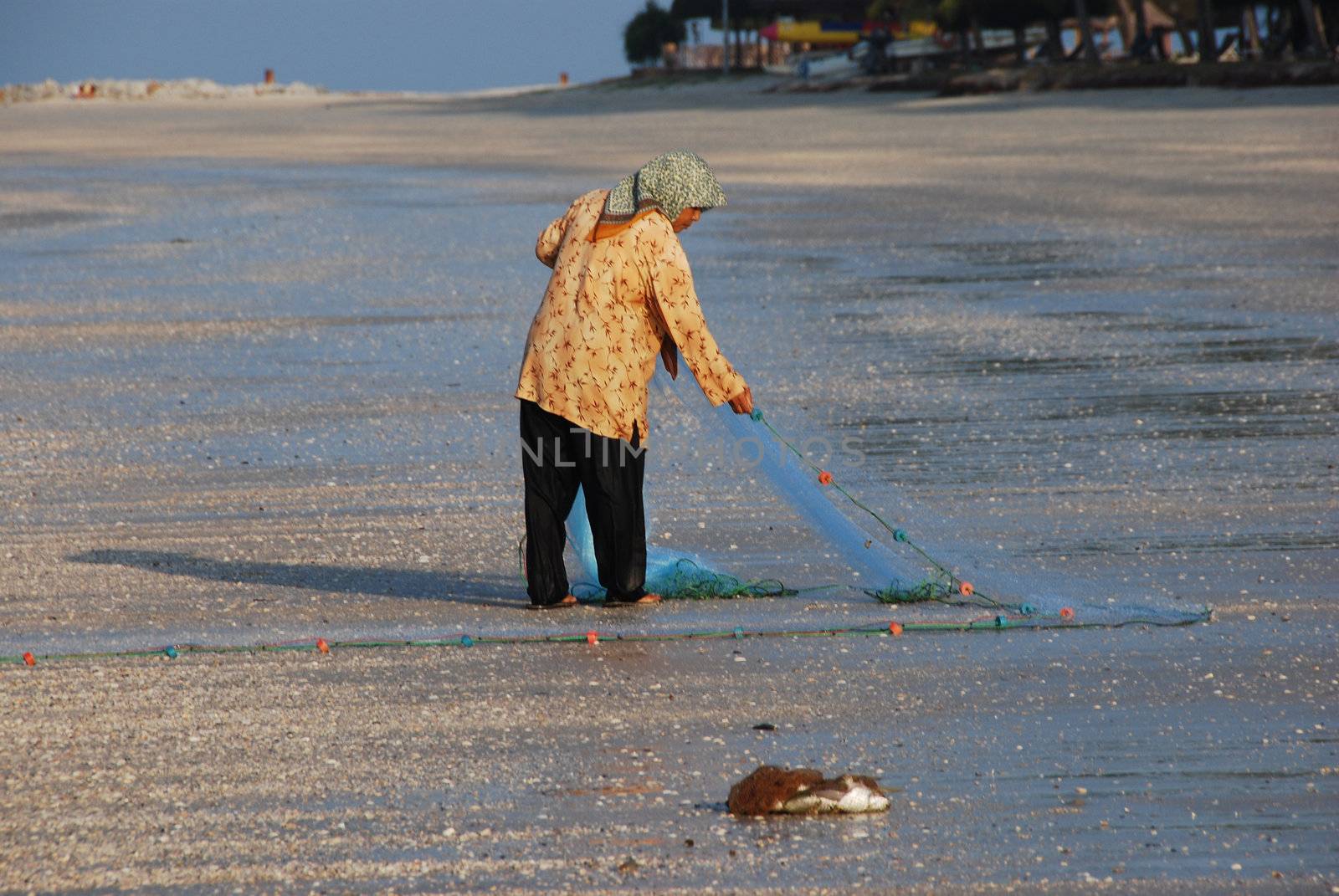 Woman sorting a fishing net on a beach