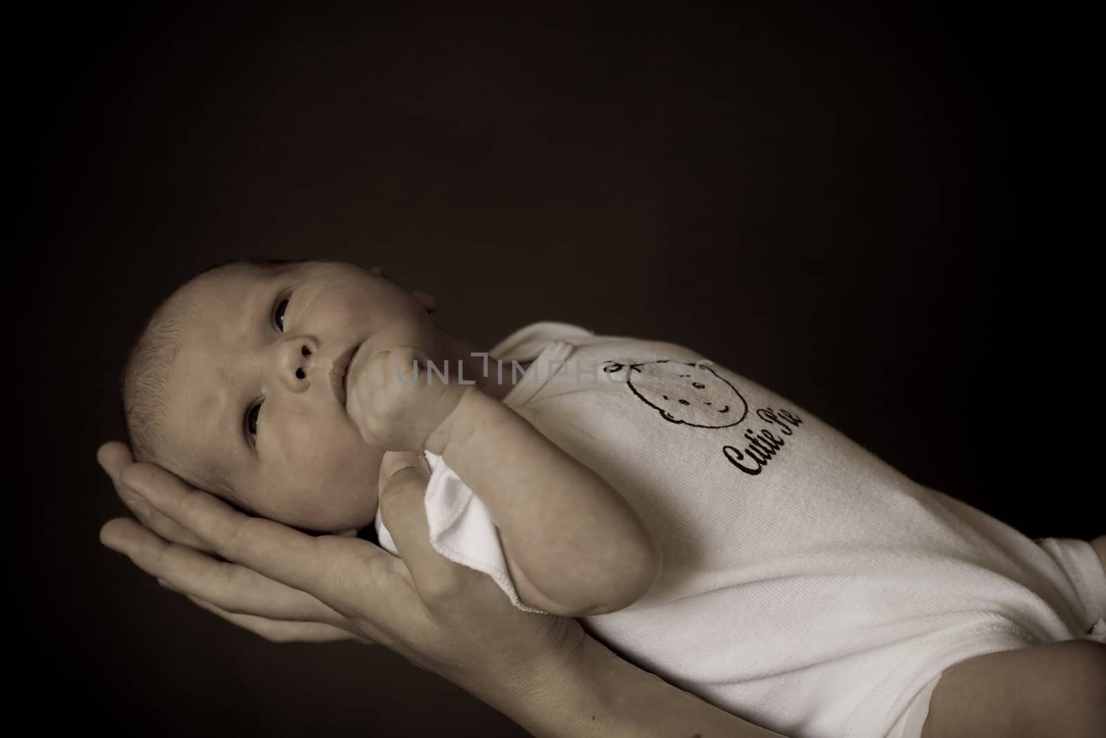 Little 7 days old baby lying securely on mom's arms, against a black background