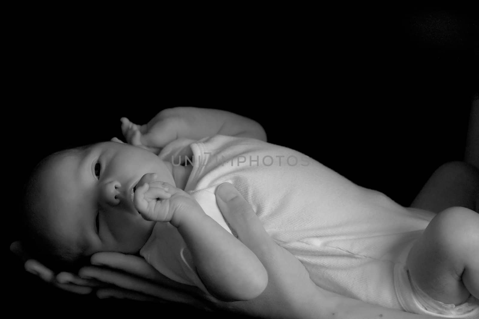 Little 7 days old baby lying securely on mom's arms, against a black background