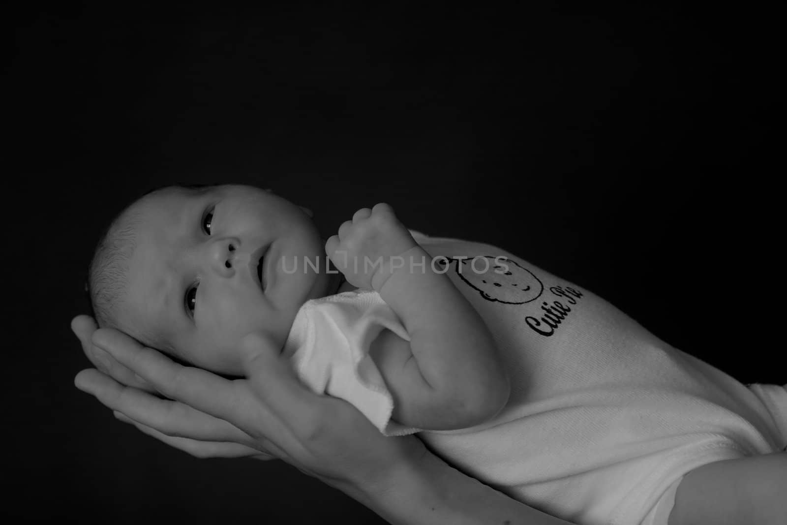 Little 7 days old baby lying securely on mom's arms, against a black background