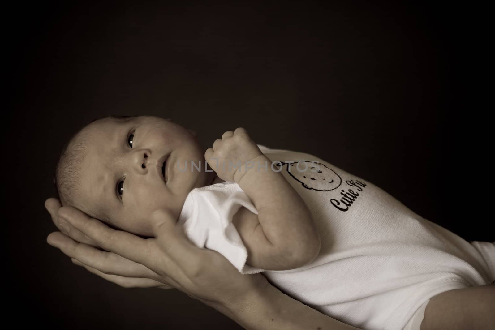 Little 7 days old baby lying securely on mom's arms, against a black background