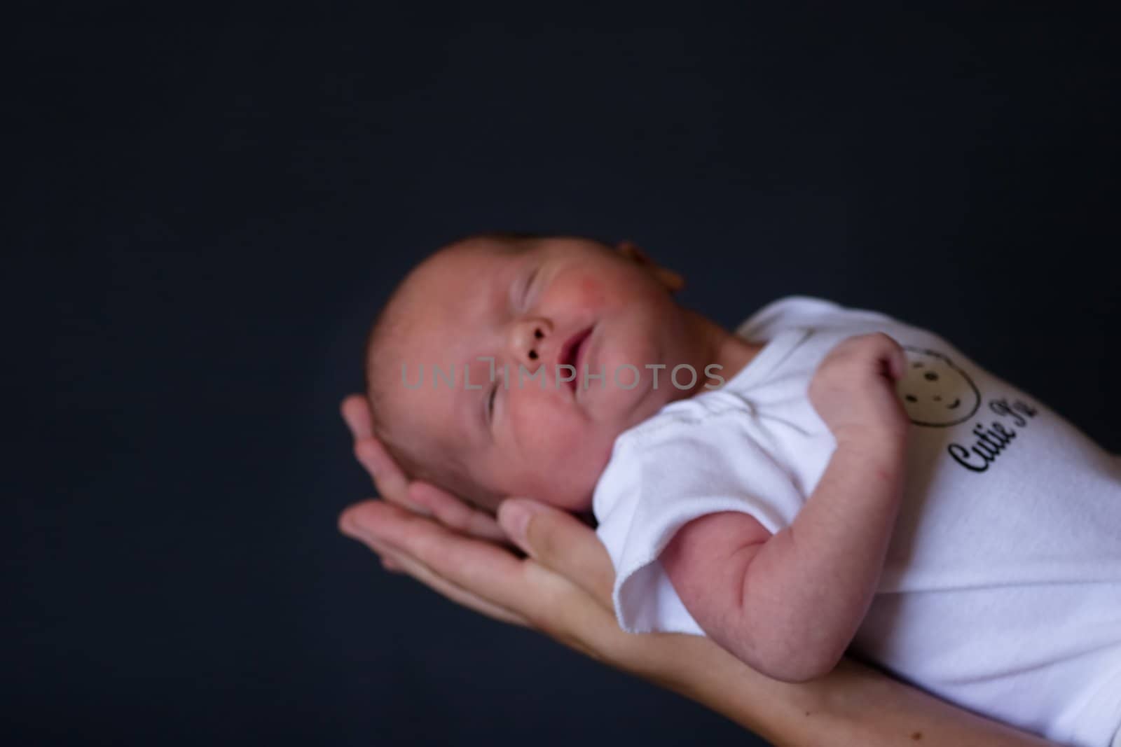 Little 7 days old baby lying securely on mom's arms, against a black background