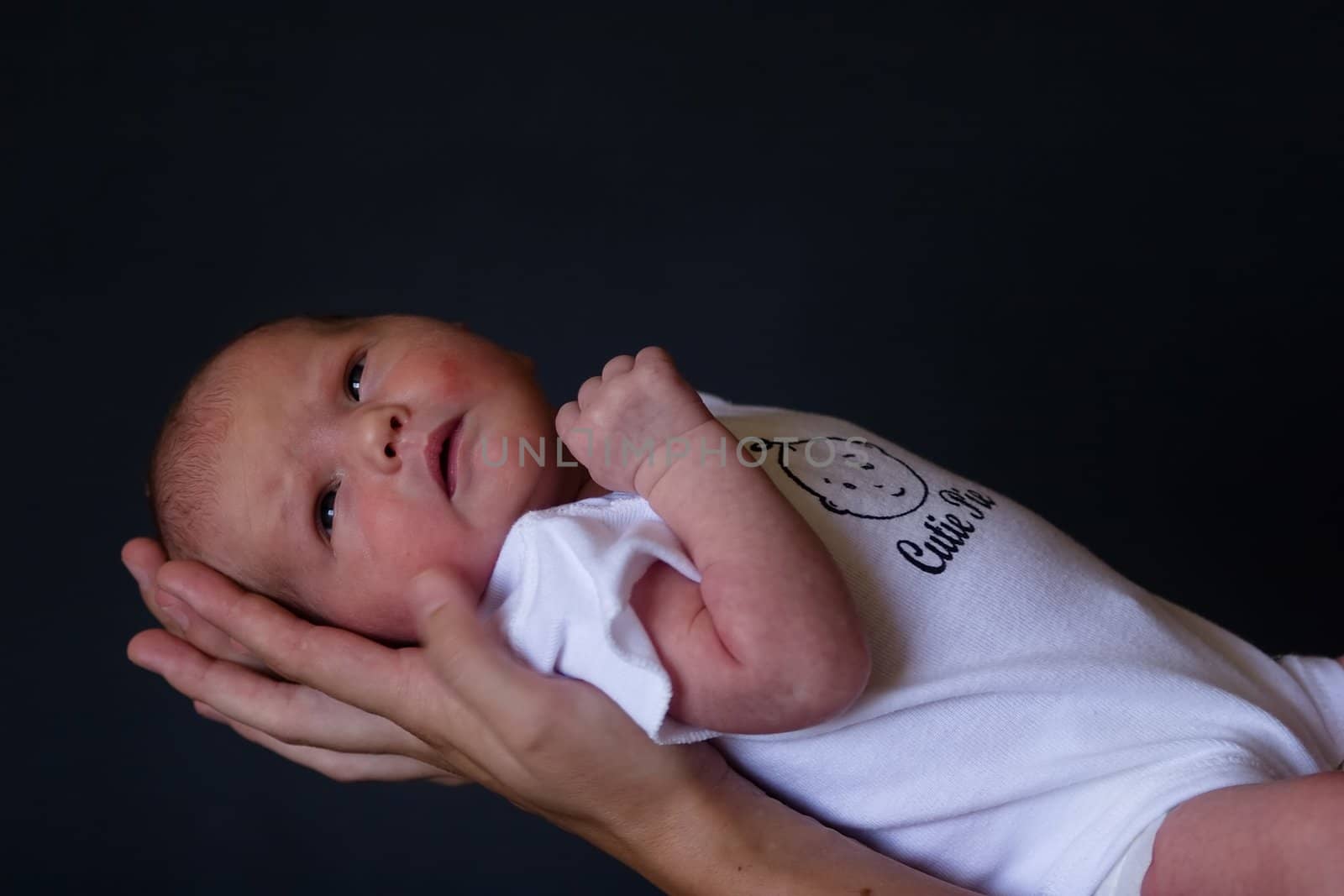 Little 7 days old baby lying securely on mom's arms, against a black background