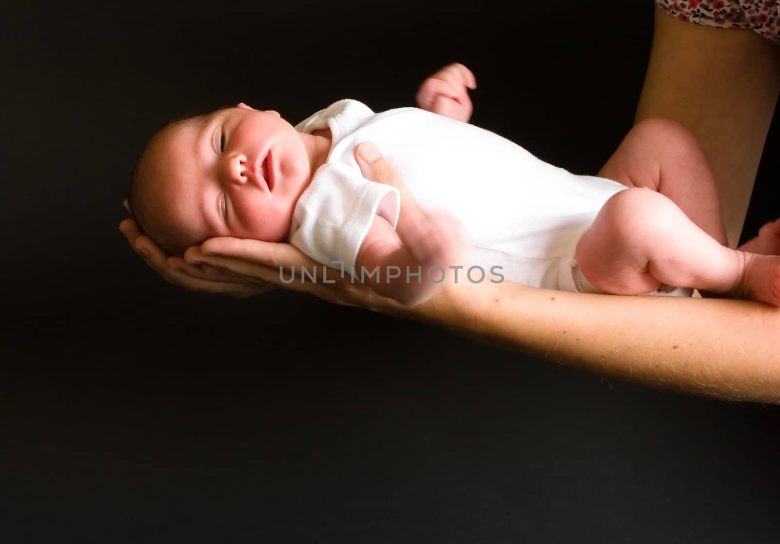 Little 7 days old baby lying securely on mom's arms, against a black background