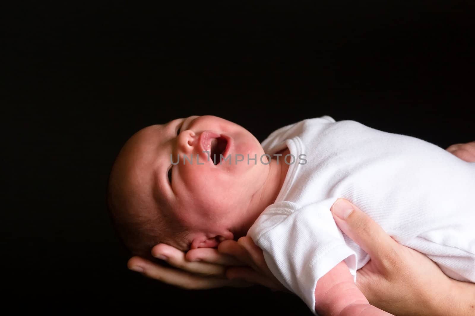 Little 7 days old baby lying securely on mom's arms, against a black background