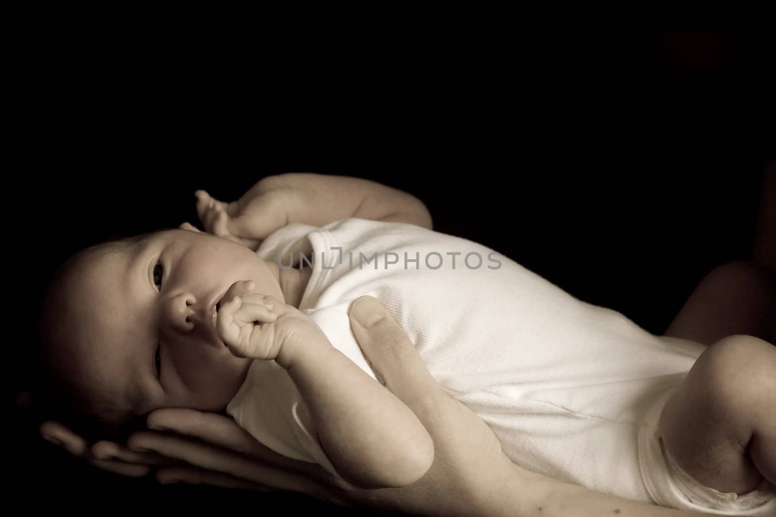 Little 7 days old baby lying securely on mom's arms, against a black background