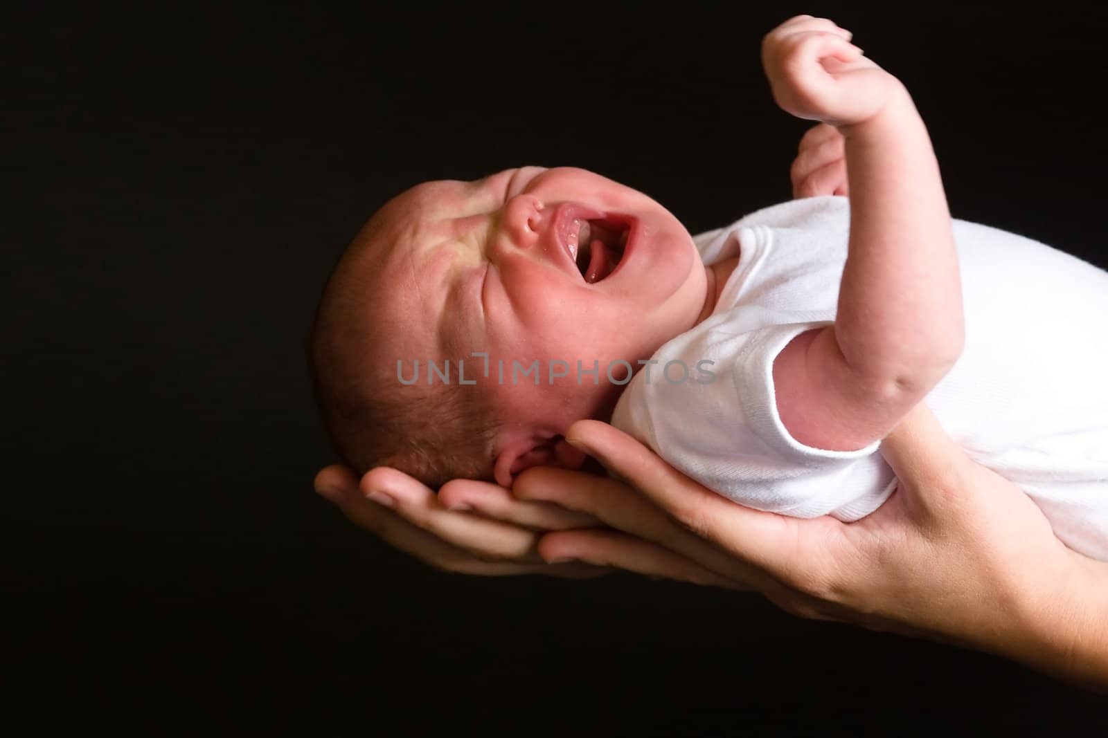 Little 7 days old baby lying securely on mom's arms, against a black background