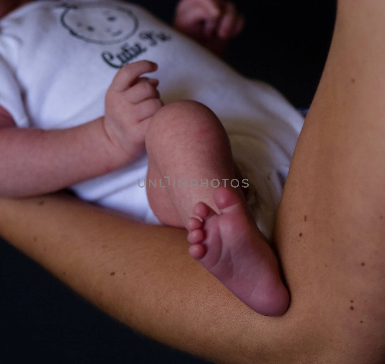 Little 7 days old baby lying securely on mom's arms, against a black background