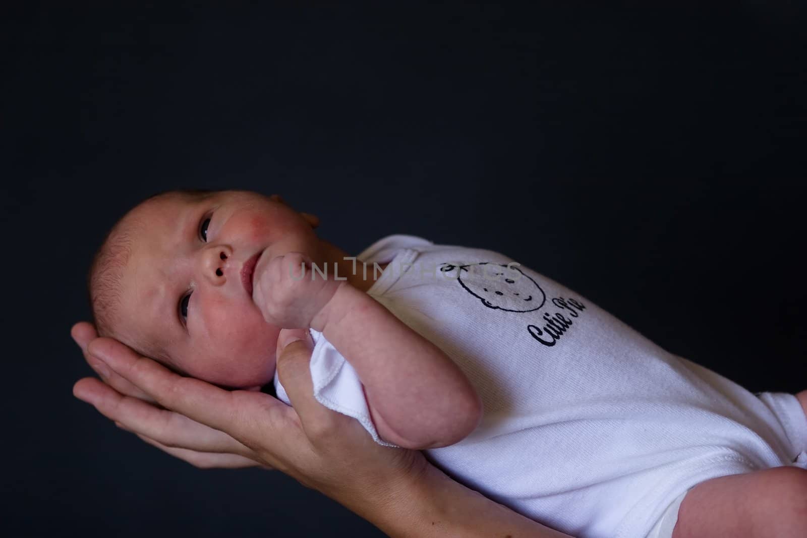 Little 7 days old baby lying securely on mom's arms, against a black background