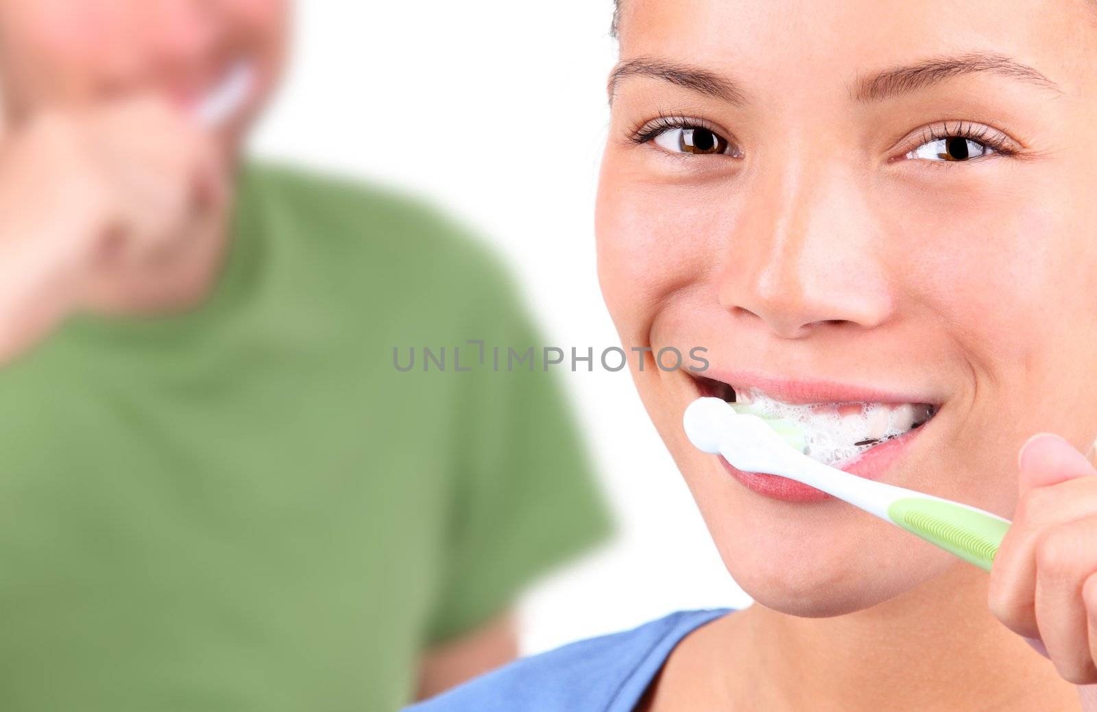 Young couple brushing teeth together on white background.