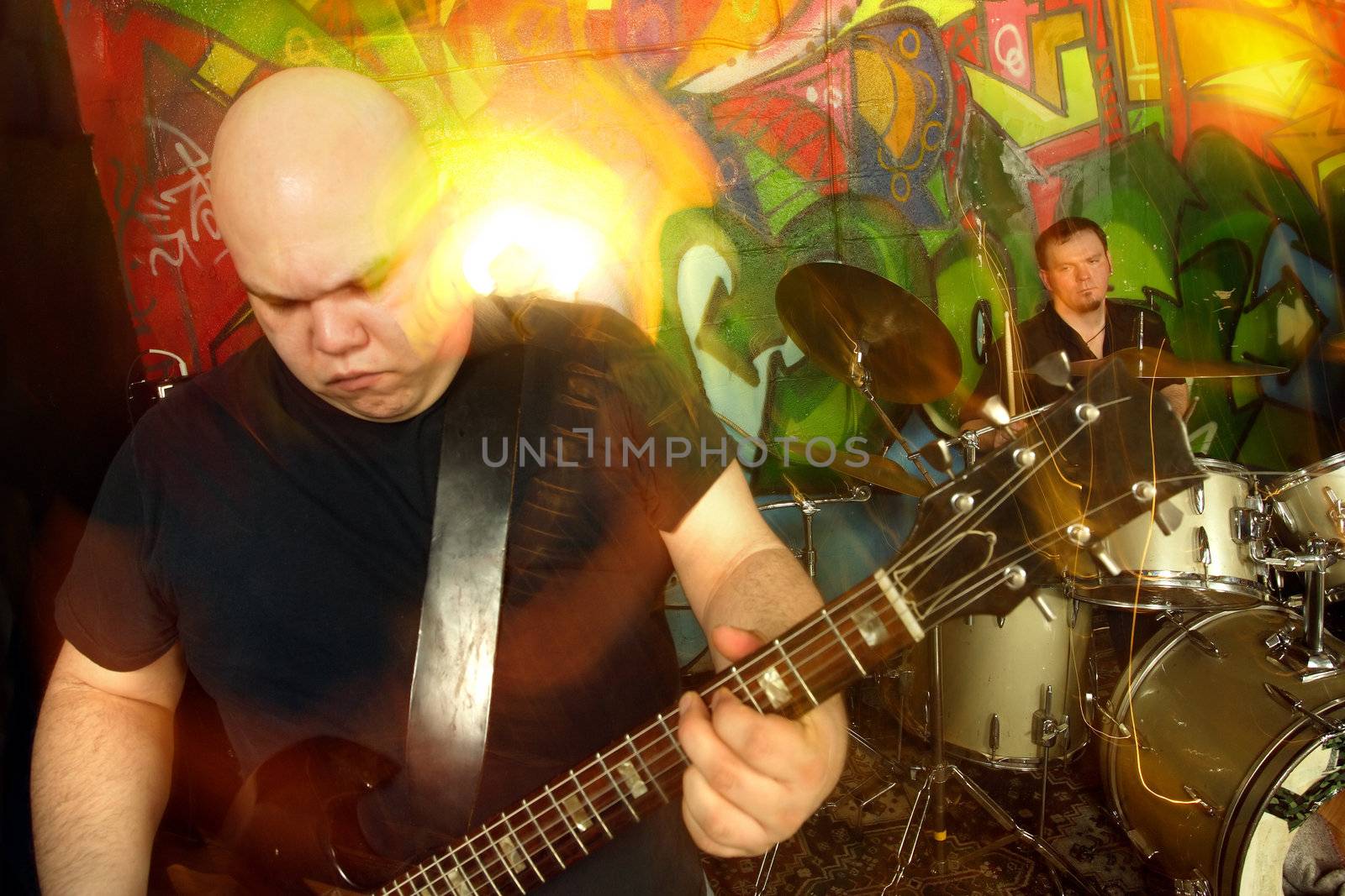 Heavy rock band playing. Shot with strobes and slow shutter speed to create lighting atmosphere and blur effects.  Slight movement visible on both players.
