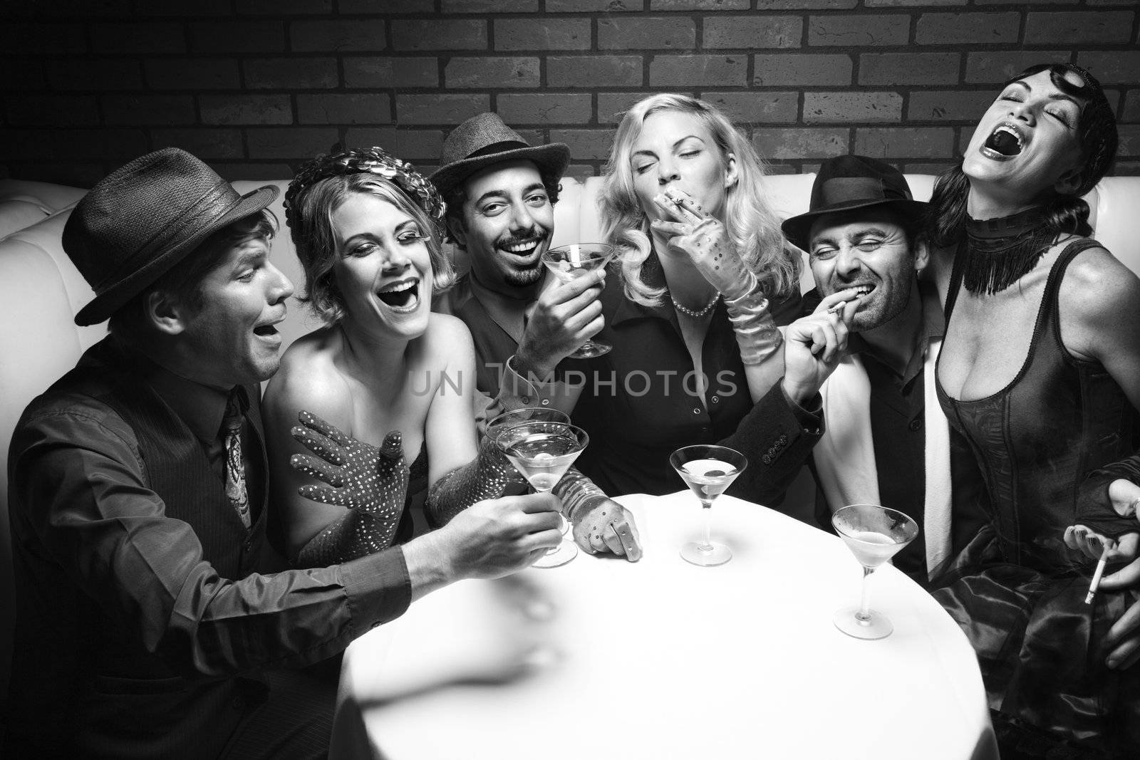Group of Caucasian prime adult retro males and females sitting at table in lounge laughing.