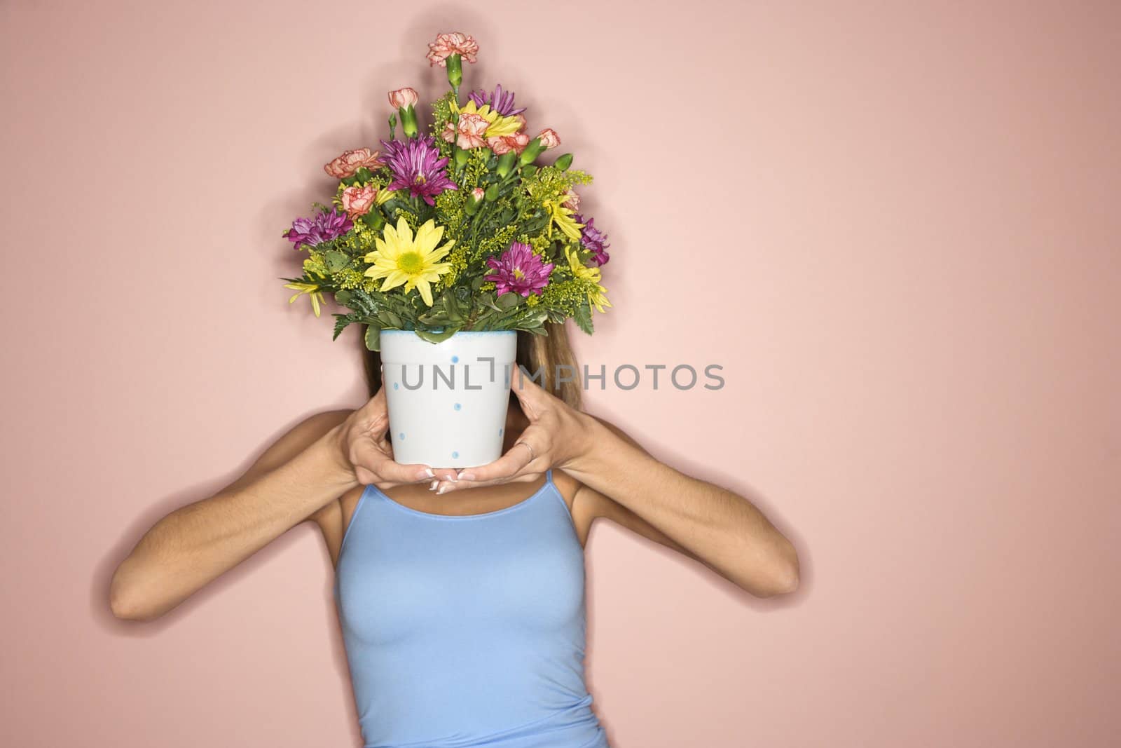 Caucasian mid-adult female holding pot of flowers in front of her face.