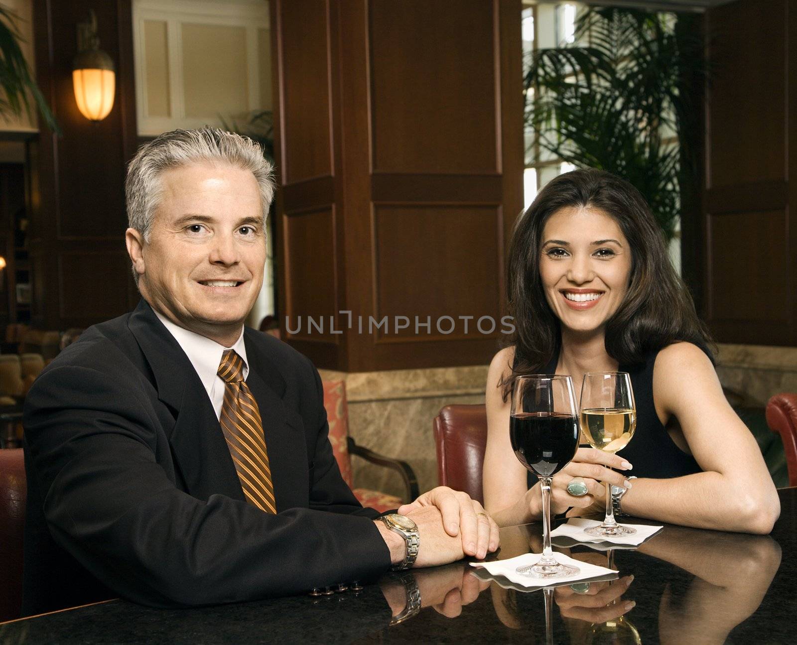 Prime adult Hispanic female and Caucasian prime adult male sitting at bar looking at viewer smiling.