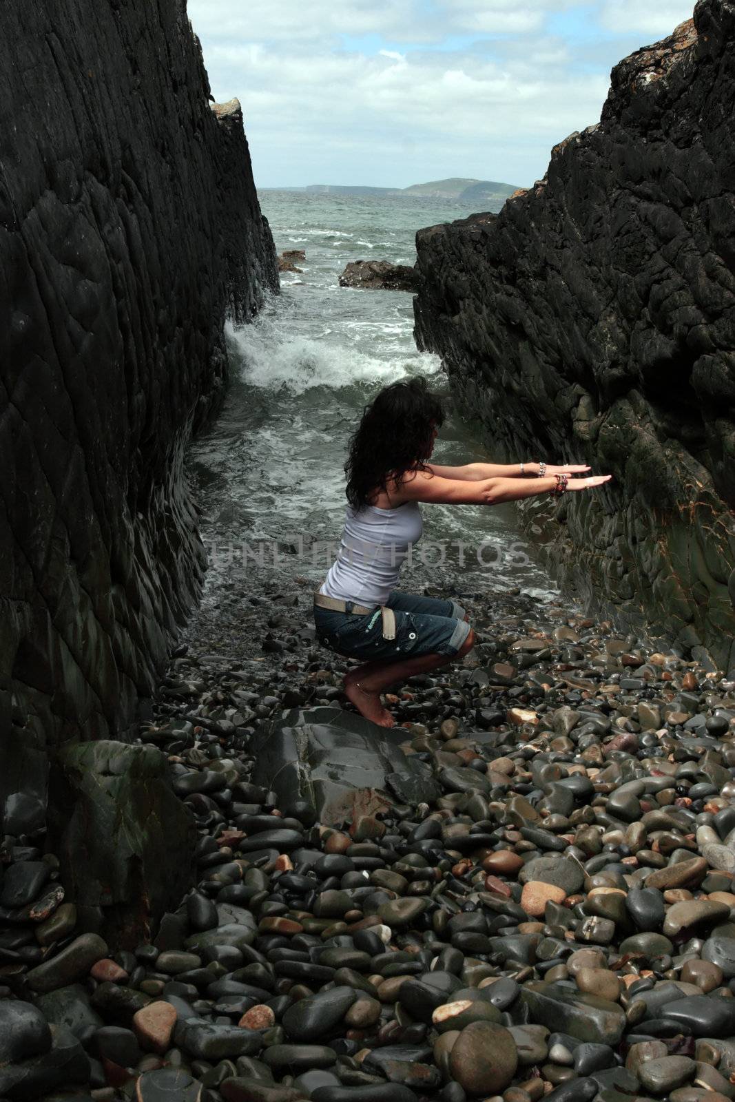 a beautiful woman practicing her yoga on the rocks in a ravine as the waves roll in