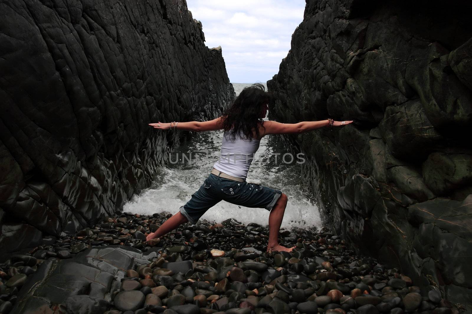 a beautiful woman practicing her yoga on the rocks in a ravine as the waves roll in