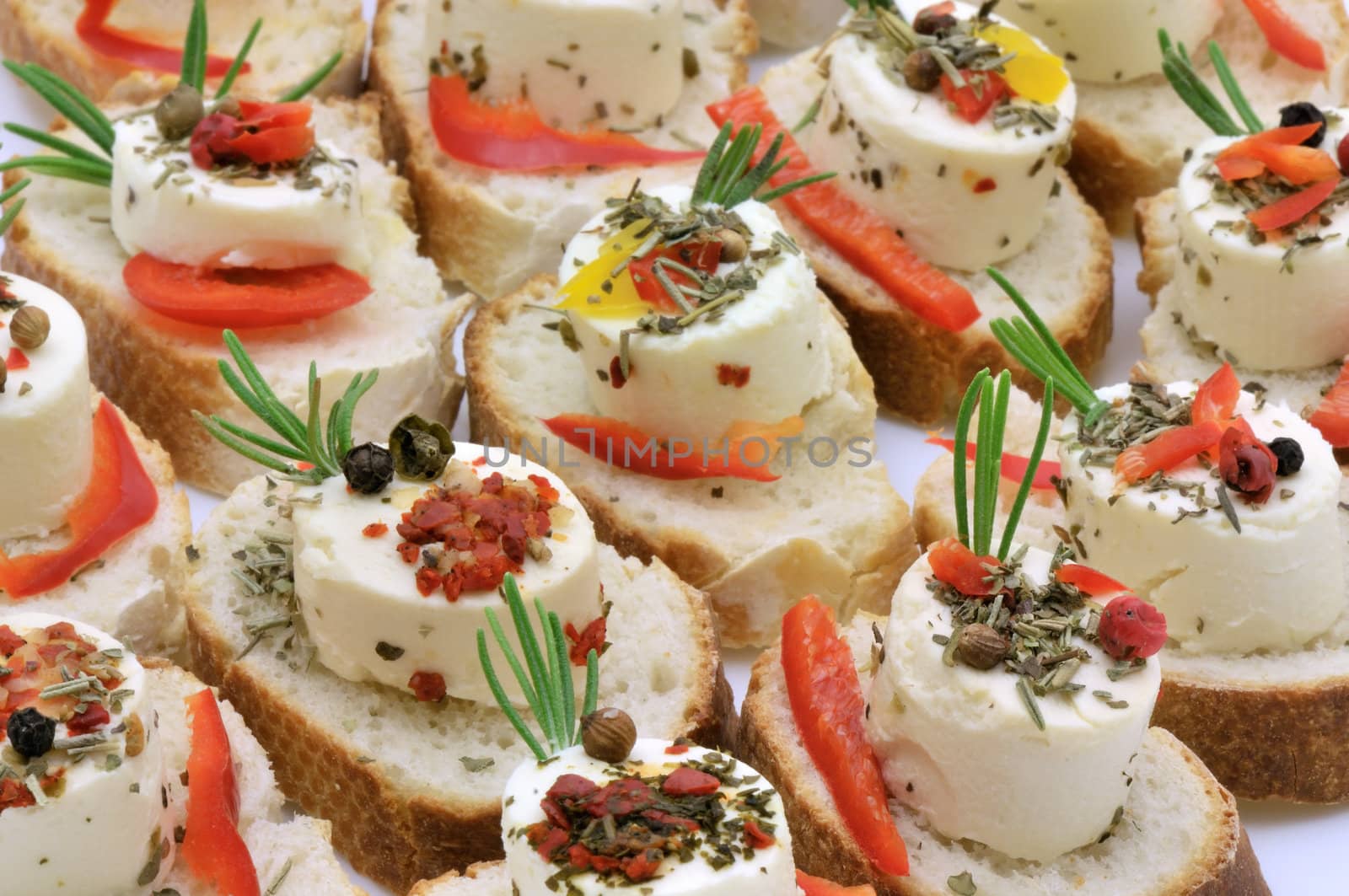 Small party cheese canapes with mediterranean flavours: fresh rosemary, mixed herbs and whole pepper