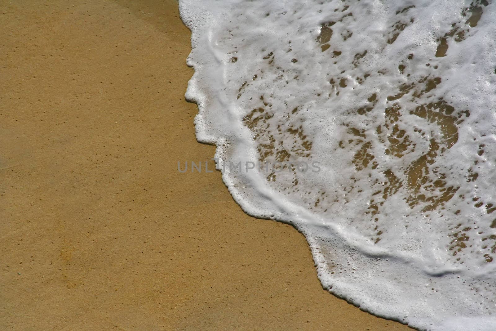 white wave in the sand at the beach by jfcalheiros