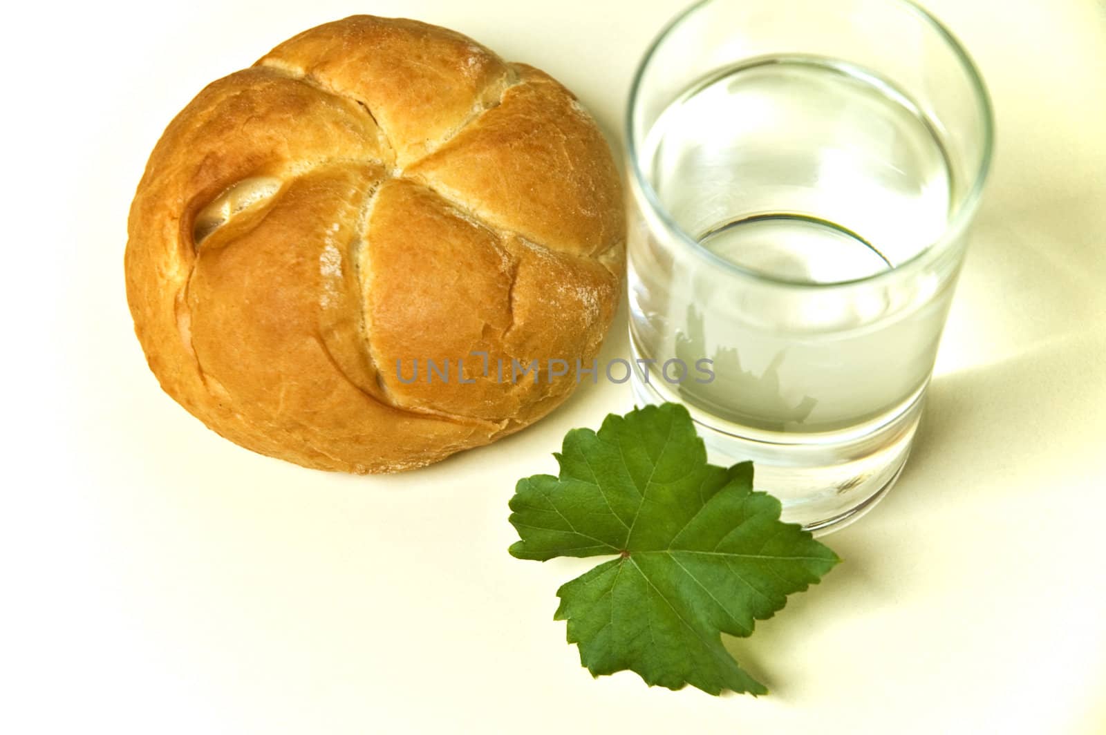 Bread roll and glass of water on kitchen table.