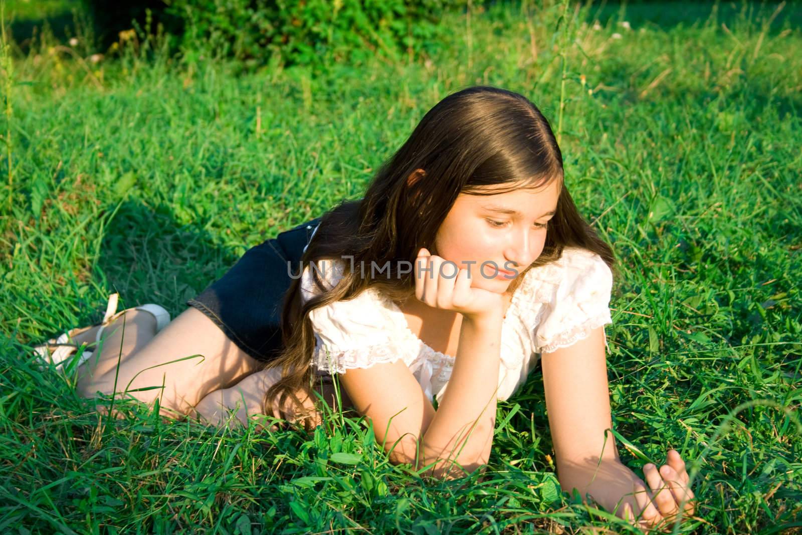 The girl lays on a green grass, thinks and smiles