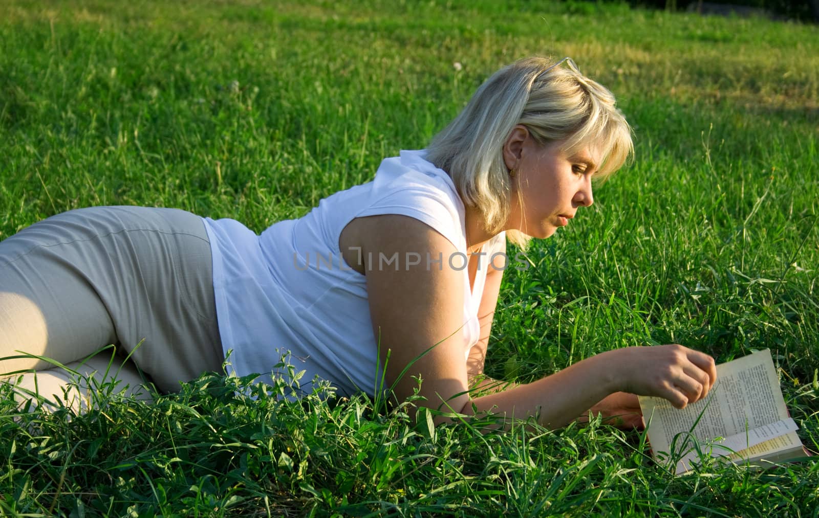 The young woman reads the book, laying on a grass