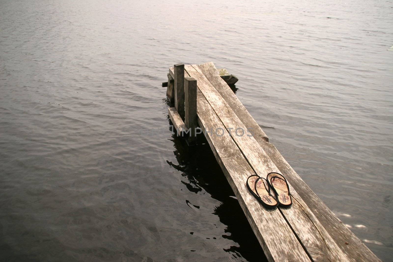 girl's flip-flops on wooden footbridge by lakeside