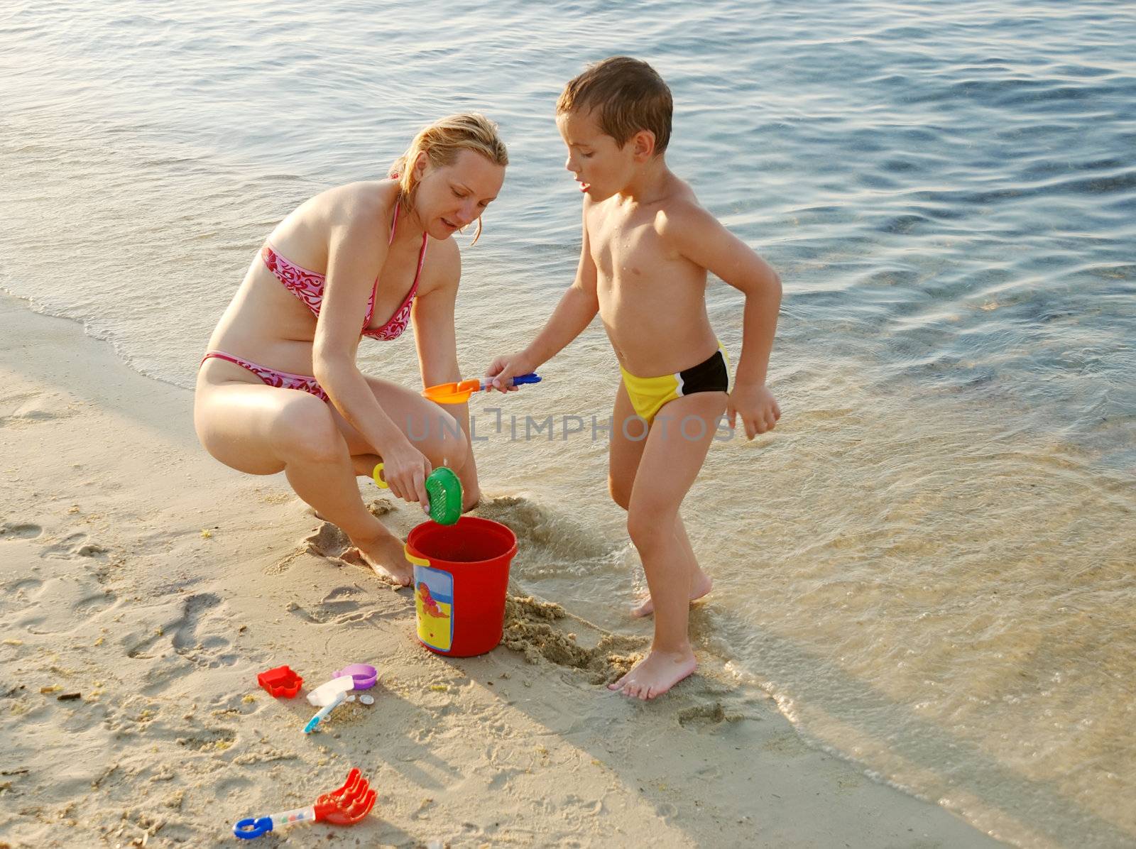 a mother and a son playing in the sand on a beach