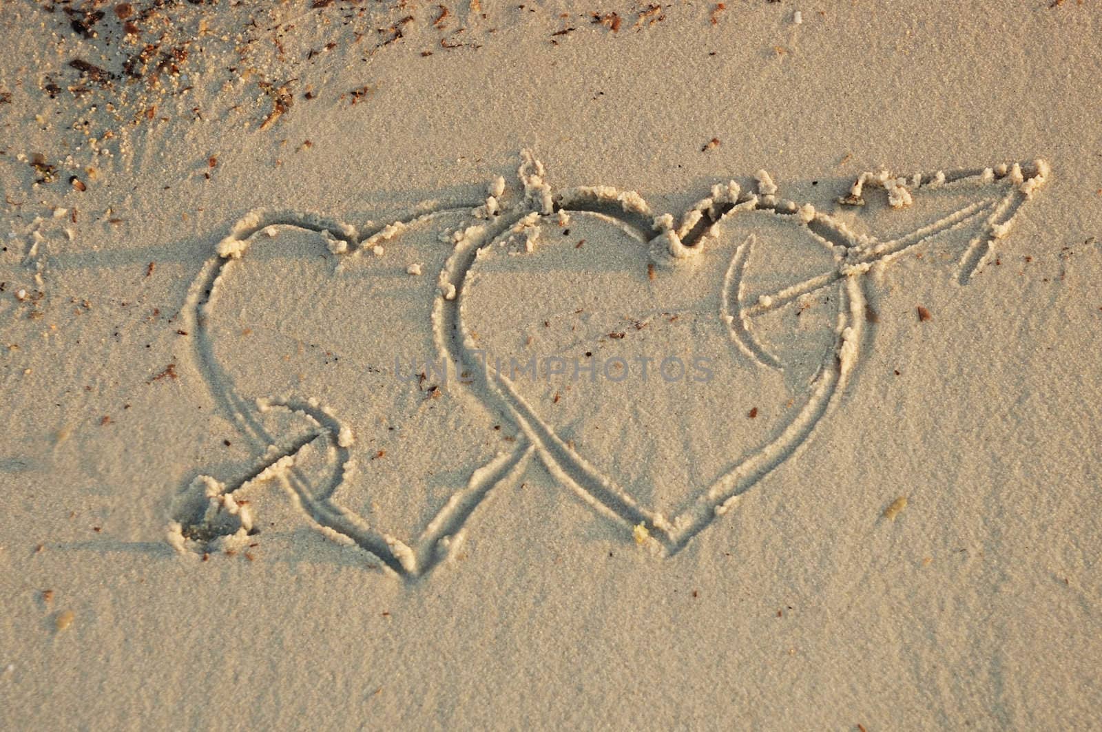 two hearts with an arrow in a sand