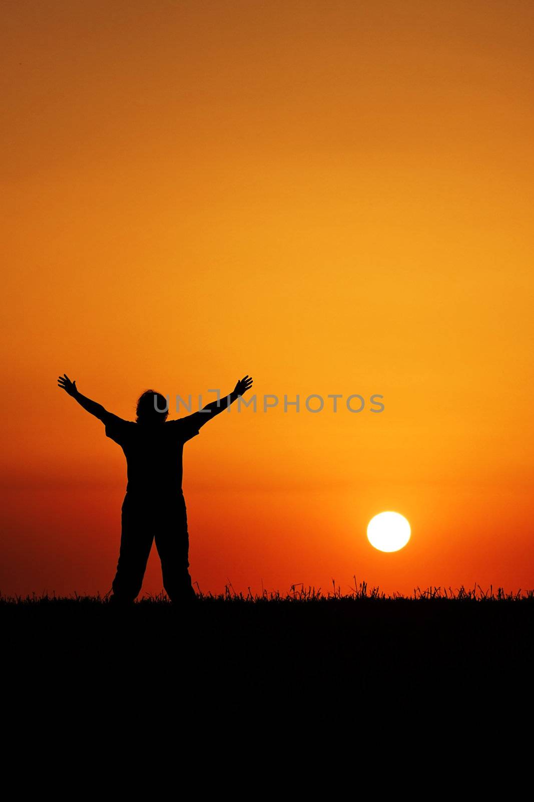 A young person with hands in air in front of beautiful blood red sunset