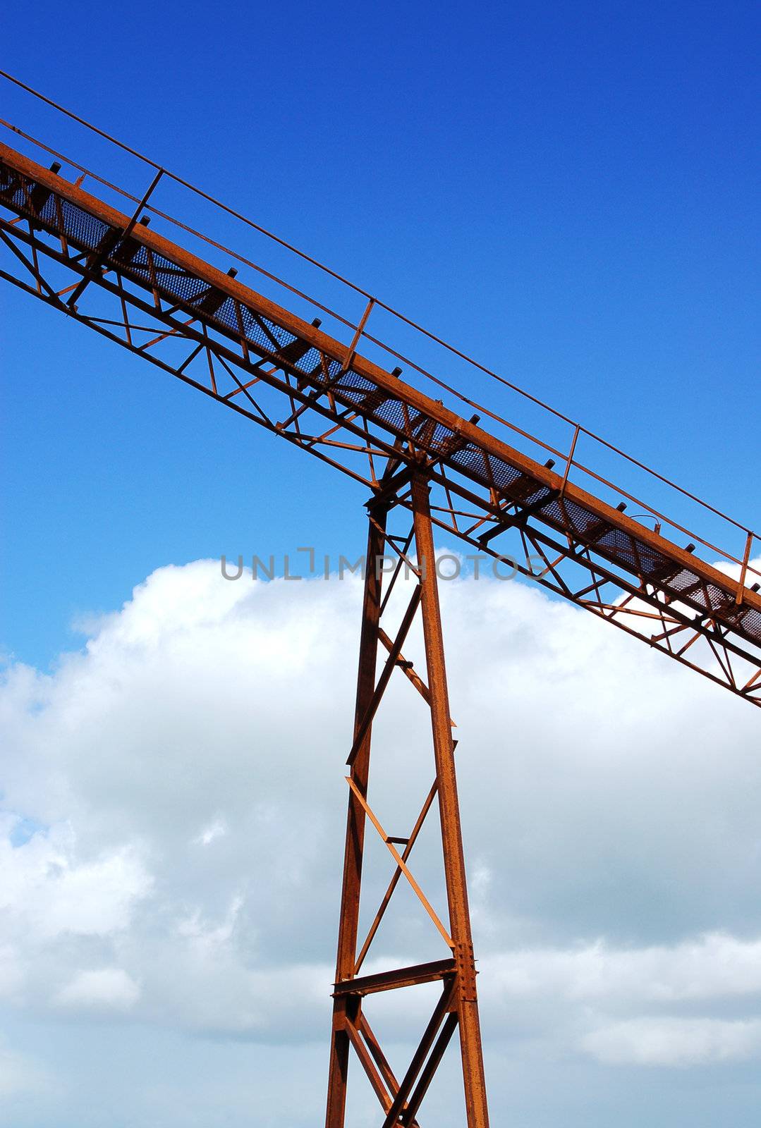 Detail of old mining conveyor belt system against blue sky background.