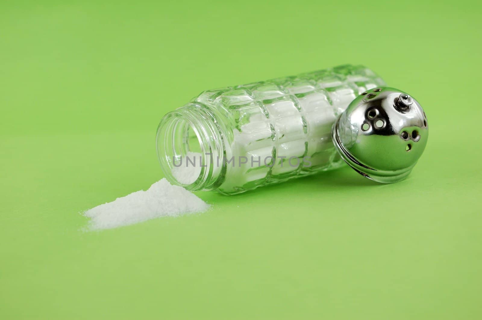 Salt poured out of glass shaker on green background.