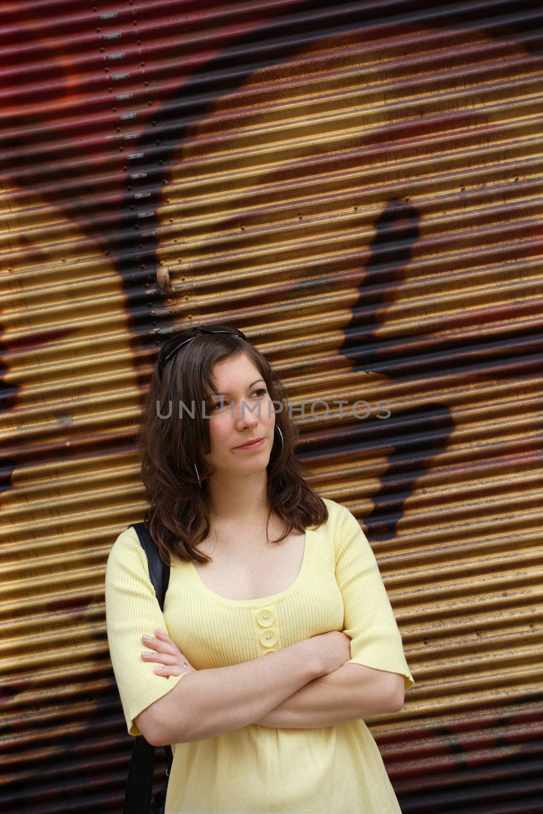 Beautiful woman standing in front of a metal pull-down door which is full of illegal graffiti.
