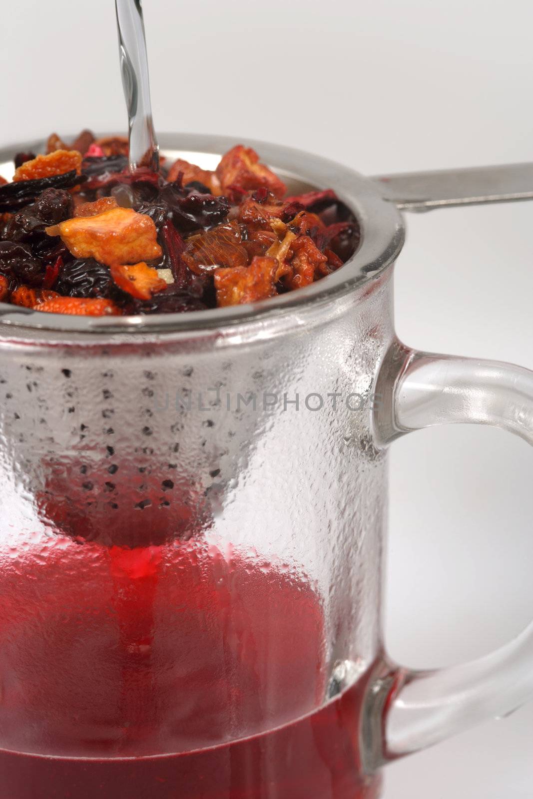 Pouring hot water through fruit tea in a metal strainer to the cup below.
